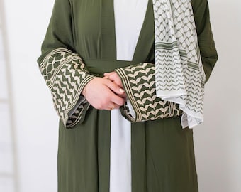 May include: An olive green abaya with intricate embroidery on the sleeves. The abaya is paired with a white and olive green patterned scarf. The sleeves have a detailed geometric design in a lighter shade, adding a touch of elegance.