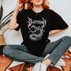 May include: Black t-shirt with a white graphic of a snake with the word "Slytherin" in a metal font.