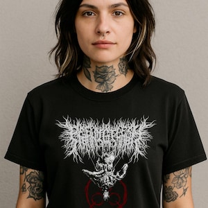May include: Black t-shirt featuring a white, stylized graphic with the text "CONQUERORS OF SHADOWS" above a skeletal figure. The design includes a red circle with a symbol. The shirt is worn by a person with tattoos.