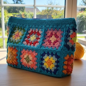 May include: A turquoise crochet bag with a zipper closure. The bag features a patchwork design of colorful granny squares in shades of pink, orange, yellow, and blue. The bag is sitting on a wooden surface.
