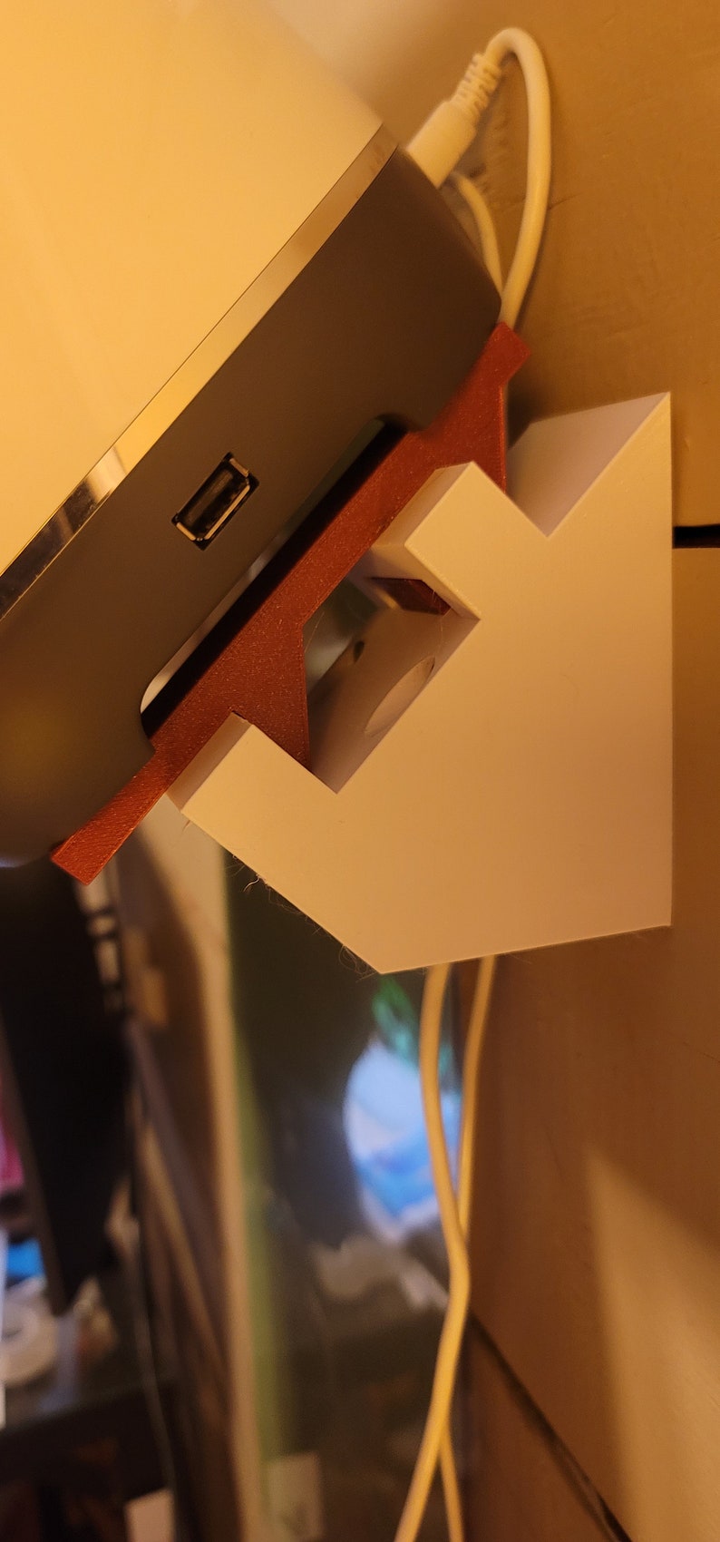 May include: A white wall mount with a red and white base, designed to hold a speaker. The speaker is light grey and white and has a USB port.
