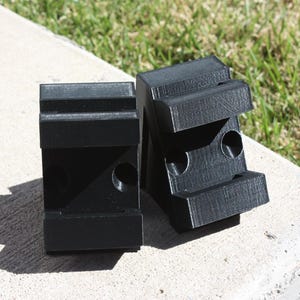 May include: Two black plastic blocks with holes and grooves. The blocks are designed to be used as mounting brackets.
