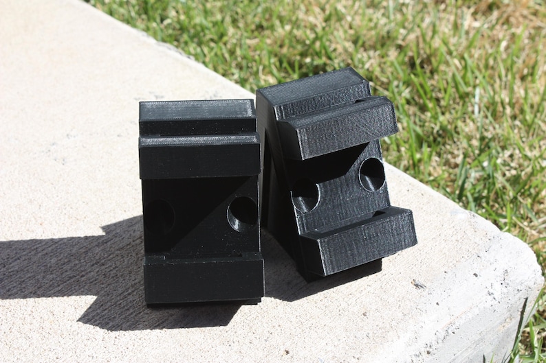 May include: Two black plastic blocks with holes and grooves. The blocks are designed to be used as mounting brackets.