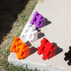 Op de afbeelding: Zes driehoekige bouwstenen in verschillende kleuren: paars, wit, oranje, rood, zwart. De blokken zijn gemaakt van plastic en hebben een getextureerd oppervlak.