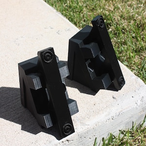 May include: Two black plastic corner brackets with a textured surface. The brackets are designed to be used for woodworking projects.