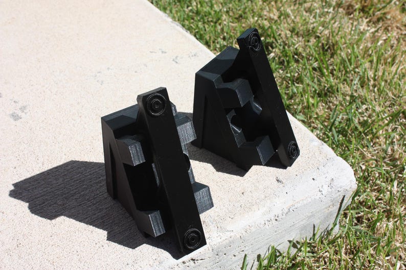 May include: Two black plastic corner brackets with a textured surface. The brackets are designed to be used for woodworking projects.