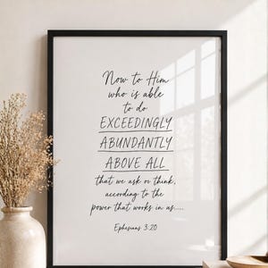 May include: A framed print with a black border featuring the text "Now to Him who is able to do exceedingly abundantly above all that we ask or think, according to the power that works in us... Ephesians 3:20." A vase with dried flowers is on the left.