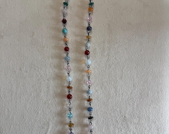 May include: A beaded necklace featuring a silver-toned metal chain interspersed with small, multi-colored beads in various shades including red, blue, green, yellow, and clear. The necklace is secured with a silver-toned metal hook clasp at the top.