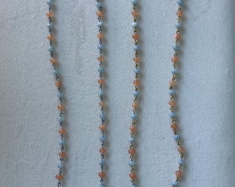 May include: Two necklaces featuring alternating light blue and orange beads strung on metal chains. Each necklace includes a single irregular white pearl-like accent bead near the bottom and is secured with a metal hook clasp at the top.