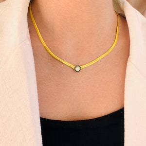 May include: A gold chain necklace with a small, octagonal pendant featuring a clear gemstone set in a black enamel frame.