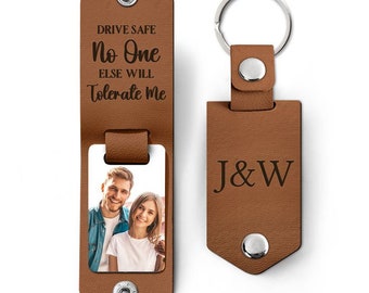 May include: Brown leather keychain with a photo insert and a personalized message that reads "Drive Safe No One Else Will Tolerate Me". The keychain also has a separate tag with the initials "J&W" engraved on it.