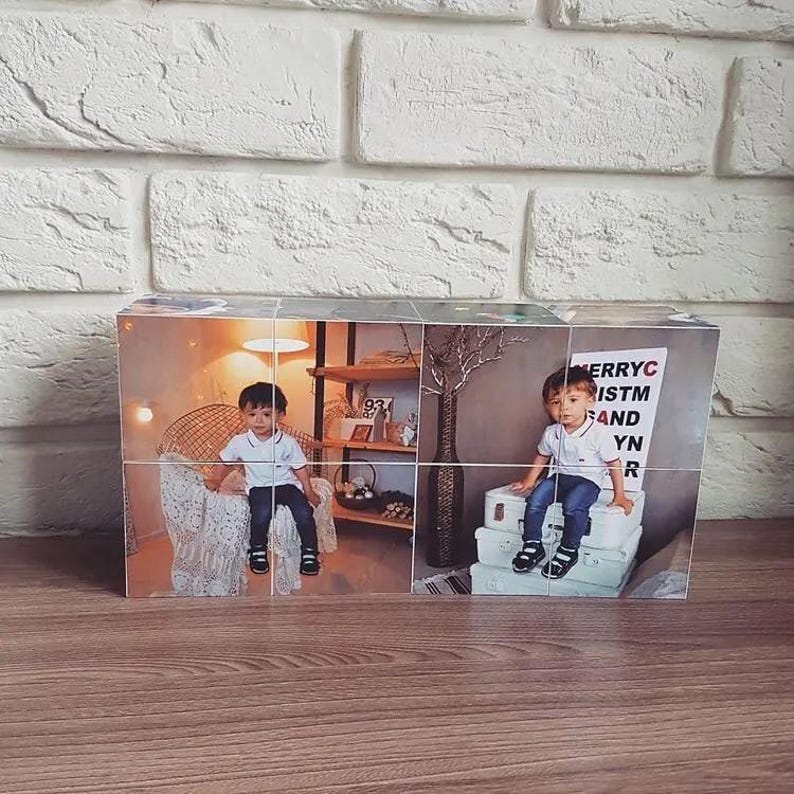Pu&ograve; includere: Un cubo fotografico in legno con un collage di immagini di un bambino piccolo. Il bambino indossa una camicia blu e jeans. Il cubo &egrave; decorato con il testo "Buon Natale e Felice Anno Nuovo".