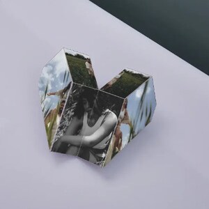 Pu&ograve; includere: Un cubo fotografico a forma di cuore con sei lati, ognuno con un'immagine diversa di persone in un campo. Le immagini sono in bianco e nero e a colori.
