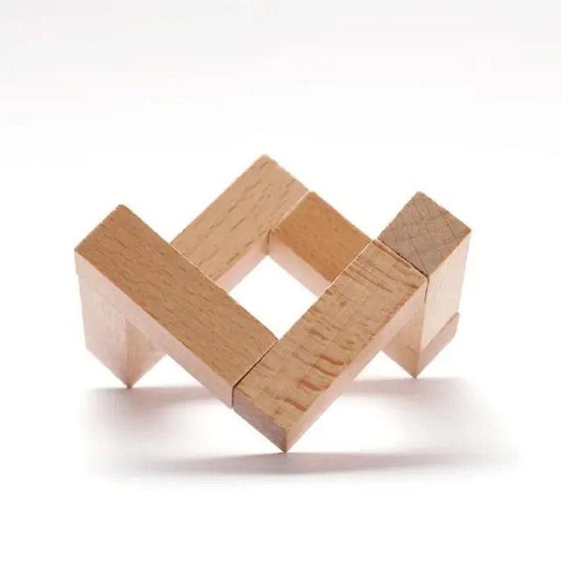 Pu&ograve; includere: Un puzzle di legno composto da quattro blocchi quadrati, ognuno con un orientamento diverso, formando una forma quadrata con un foro al centro.