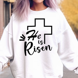 May include: White sweatshirt with a black cross and the text "He is Risen" printed on the front.