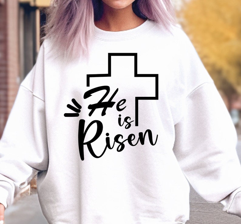 May include: White sweatshirt with a black cross and the text "He is Risen" printed on the front.