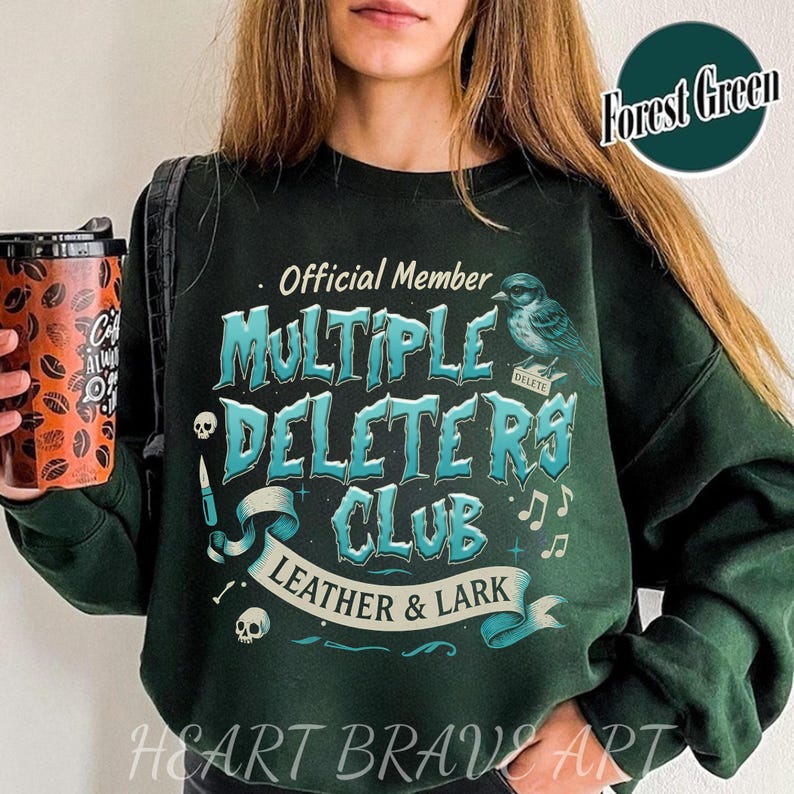May include: A dark green sweatshirt with the text "Official Member Multiple Deletors Club Leather & Lark" in a blue and white font. The text is surrounded by a decorative banner and a small bird graphic. The text "Forest Green" is in a white box in the upper right corner of the image.