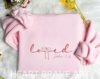 May include: Pink sweatshirt with the word "loved" in cursive with a bow in the middle and the text "John 3:16" below the bow.