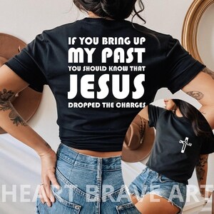May include: Black t-shirt with white text that reads "If you bring up my past you should know that Jesus dropped the charges". A second black t-shirt with a white cross and the word "Jesus" is visible in the background.