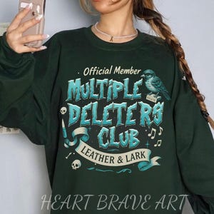 May include: Green sweatshirt with a blue and white graphic design that says "Official Member Multiple Deleters Club Leather & Lark" with a bird and musical notes.