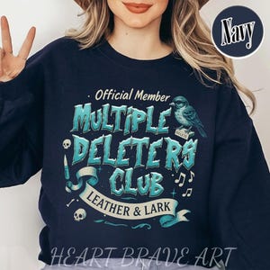 May include: A navy blue sweatshirt with a graphic design that says "Official Member Multiple Deleters Club Leather & Lark". The graphic features a blue bird with a "Delete" tag on its leg, musical notes, and skulls.