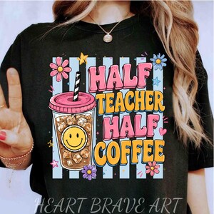 Puede incluir: Una camiseta negra con un gráfico de un vaso de café helado con una cara sonriente, rodeado de flores y estrellas. El texto HALF TEACHER HALF COFFEE aparece en letras de burbuja rosas y amarillas sobre un fondo de rayas verticales azul claro.