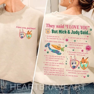 May include: Beige sweatshirt with the text "I love you, partner!" and a cartoon image of a bunny and fox. The back of the sweatshirt has text that says "They said 'I LOVE YOU' But Nick & Judy Said..." with a list of quotes.
