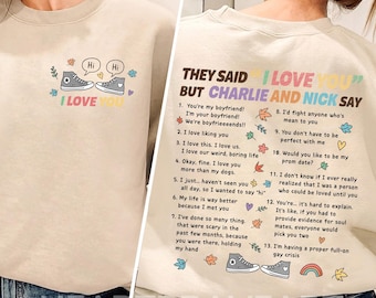 Könnte beinhalten: Beiges Sweatshirt mit dem Text "I LOVE YOU" und einer Grafik von zwei Turnschuhen mit Sprechblasen. Auf der Rückseite des Sweatshirts befindet sich eine Liste von Sätzen und der Text "THEY SAID I LOVE YOU BUT CHARLIE AND NICK SAY".