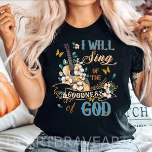 May include: Black t-shirt with a floral design featuring a guitar and butterflies. The text "I Will Sing of the Goodness of God" is printed on the shirt.