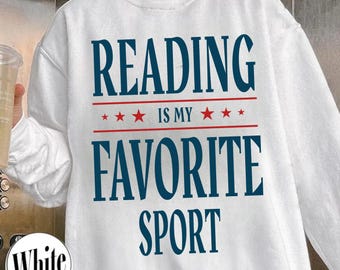 May include: White sweatshirt with the text "READING IS MY FAVORITE SPORT" in navy blue, with red stars and lines. The sweatshirt has long sleeves and a crew neck. The word "White" is printed on a small circle on the bottom left.