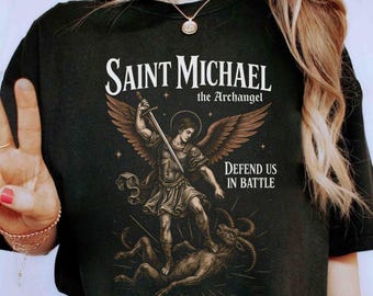 May include: Black t-shirt with a graphic of Saint Michael the Archangel slaying a demon. The graphic is in a vintage style with gold and brown accents. The text "Defend us in battle" is printed below the graphic. The text "Heart Brave Art" is printed at the bottom of the shirt.