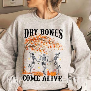 May include: Gray sweatshirt with a graphic of three skeletons dancing under a fall tree with the text "Dry Bones Come Alive".