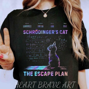 May include: Black t-shirt with the text "Schrödinger's Cat", a cat illustration, and mathematical equations. The phrase "The Escape Plan" is below the cat image. The shirt also includes the text "Heart Brave Art".