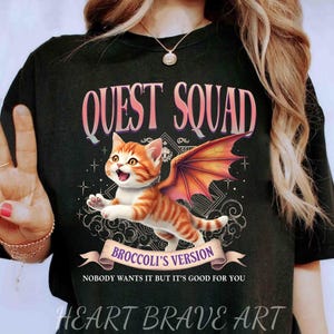 May include: Black t-shirt with a graphic of a cat with wings. The text "QUEST SQUAD" is above the cat and "BROCCOLI'S VERSION" is below the cat. The text "NOBODY WANTS IT BUT IT'S GOOD FOR YOU" is below the graphic.