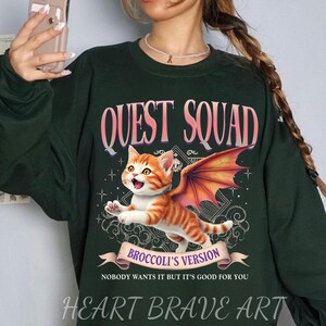May include: Green sweatshirt with a graphic of a cat with wings. The text "QUEST SQUAD" is above the cat and "BROCCOLI'S VERSION" is below the cat. The text "NOBODY WANTS IT BUT IT'S GOOD FOR YOU" is below the graphic.