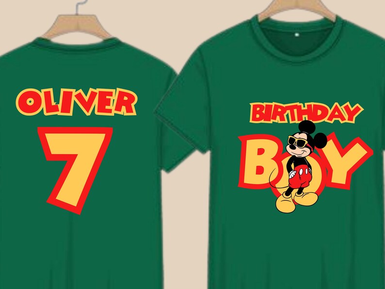 May include: Two dark green t-shirts featuring yellow and red text and graphics. One shirt displays the name OLIVER above the number 7. The other shirt features the text BIRTHDAY BOY with a graphic of Mickey Mouse wearing sunglasses.