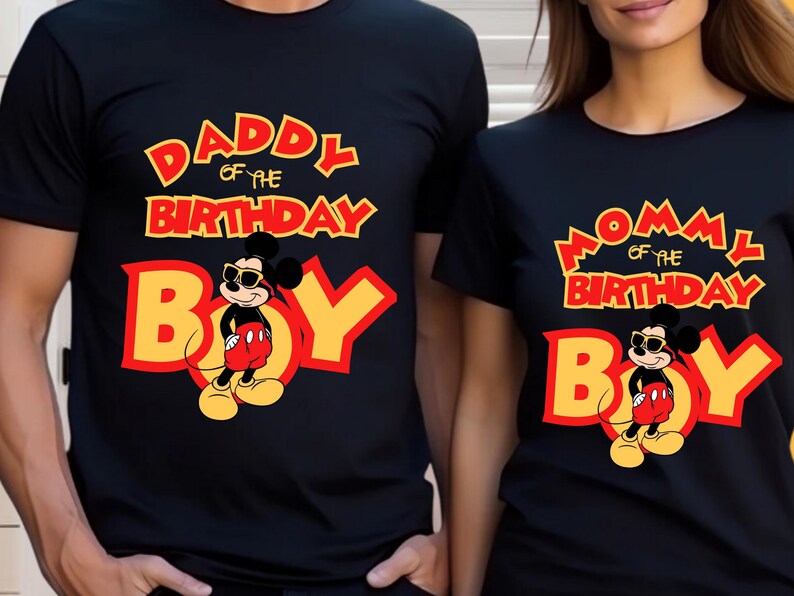 May include: Two black short-sleeved t-shirts featuring a graphic of Mickey Mouse wearing sunglasses. One shirt displays the text "DADDY OF THE BIRTHDAY BOY" in yellow and red, while the other shirt displays "MOMMY OF THE BIRTHDAY BOY" in the same colors.