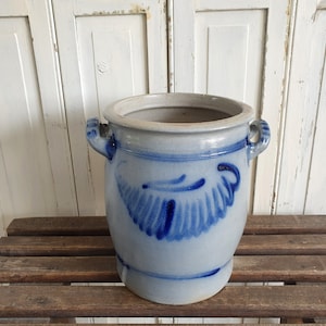 May include: A blue and white ceramic crock with two handles. The crock has a blue and white floral design.