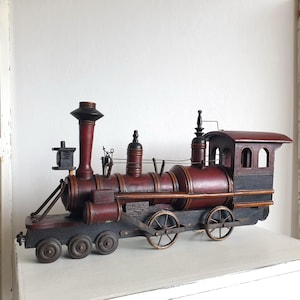 Könnte beinhalten: Eine dekorative hölzerne Modelleisenbahn-Lokomotive in dunkelroter und schwarzer Farbgebung. Das Modell verfügt über einen hohen Schornstein, ein Führerhaus mit Bogenfenstern und mehrere Speichenräder, die ein detailliertes, historisches Design aufweisen.