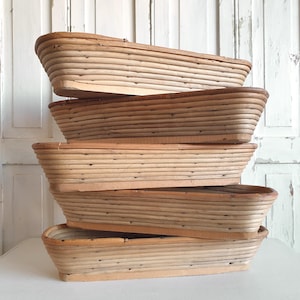 May include: Five rectangular wooden bread proofing baskets stacked on top of each other. The baskets are made of woven light-coloured wood strips, with a rounded rim and a flat base. The baskets are of various sizes and shapes.
