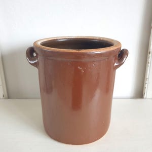 Può includere: Un vaso di terracotta marrone con due manici. Il vaso ha una finitura smaltata ed è in stile rustico.