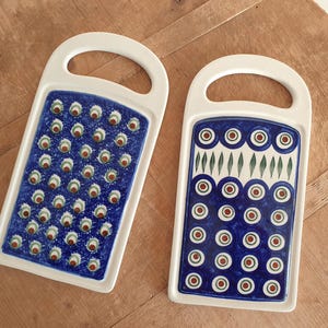 May include: Two white ceramic chopping boards with blue and green designs. One board has a pattern of small circles with a white centre, the other has a pattern of larger circles with a red centre.