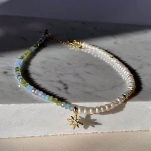 May include: A delicate gold necklace with a star charm. The necklace is made of small white pearls and green, blue, and clear glass beads.