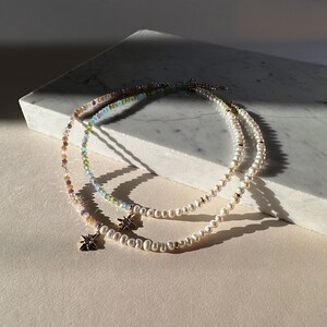 May include: Two delicate necklaces with starburst charms. One necklace is made of white pearls and the other is made of multi-colored beads.