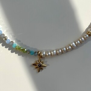 May include: A delicate necklace with a gold star charm and a mix of blue and white beads.