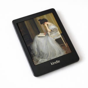 May include: Black Kindle e-reader displaying a painting of a woman reading. The painting shows a woman in a long, flowing dress seated in a chair. The e-reader has a black border and the word "kindle" is printed at the bottom.