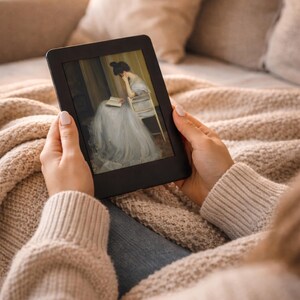 May include: A black e-reader displaying a classical painting of a woman in a long, flowing dress, seated and reading. The e-reader is held by a person wearing a beige sweater, resting on a beige blanket and pillows.
