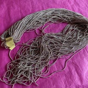 May include: A long, multi-strand necklace featuring numerous thin, metallic silver-toned snake chains gathered together and secured by a single, rectangular, polished gold-toned metal clasp, creating a cascading, fluid, and textured appearance.