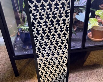 May include: A black metal planter with a white geometric pattern. The planter has a rectangular shape and is tall and narrow.