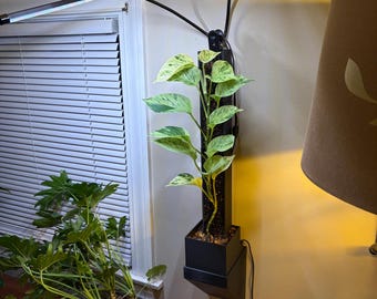 May include: A black, wall-mounted plant stand with a built-in LED grow light. The stand holds a pothos plant with green and white variegated leaves. A second plant in a wooden planter sits on a wooden surface.